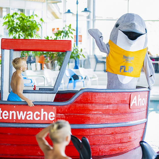 Flip winkt und Kinder spielen im Kinderbereich